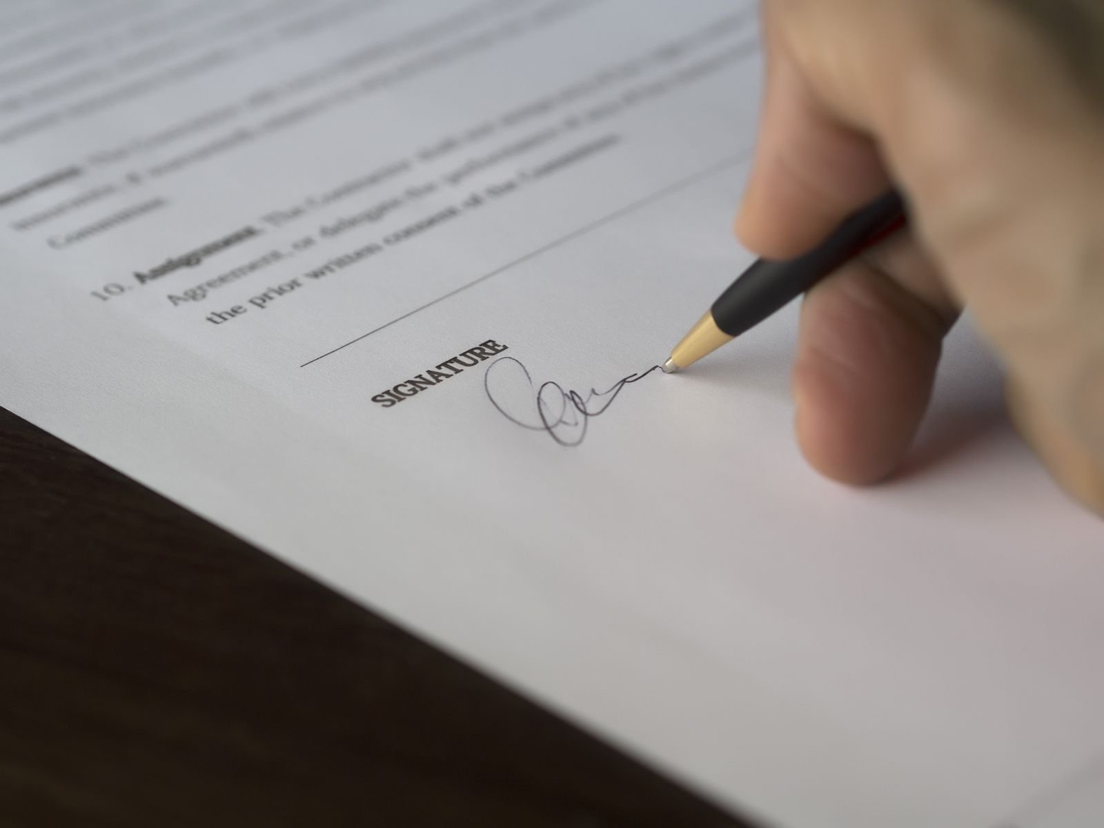 A hand signing a formal legal contract with a pen on a wooden desk