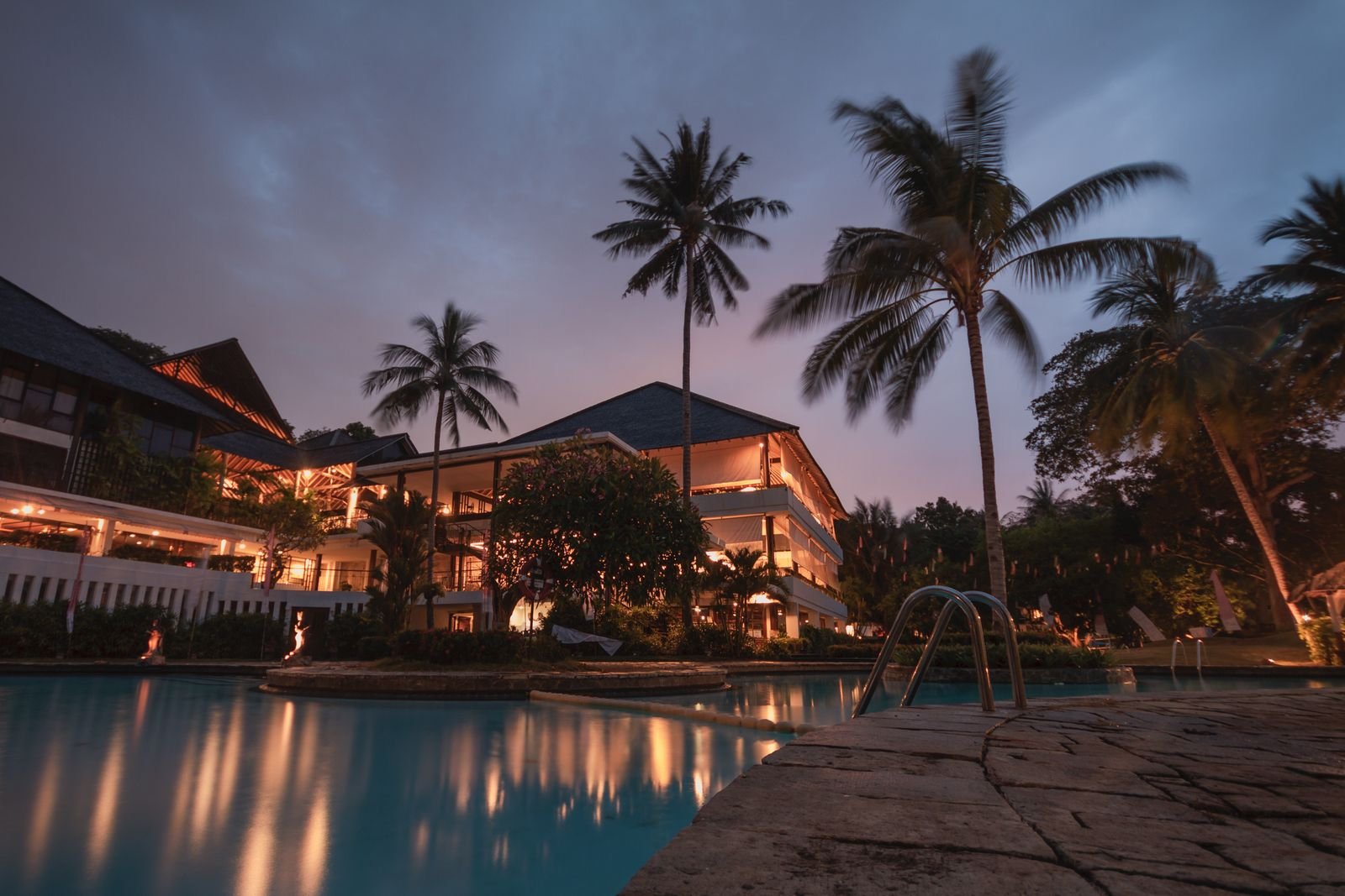 A resort swimming pool surrounded by palm trees at dusk
