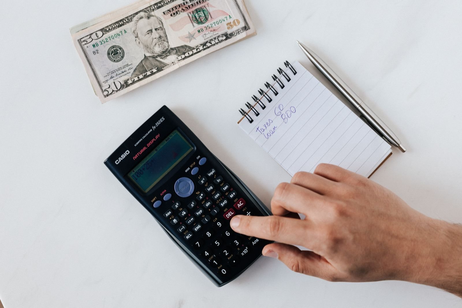 Overhead view of hands using a calculator over a notepad and cash